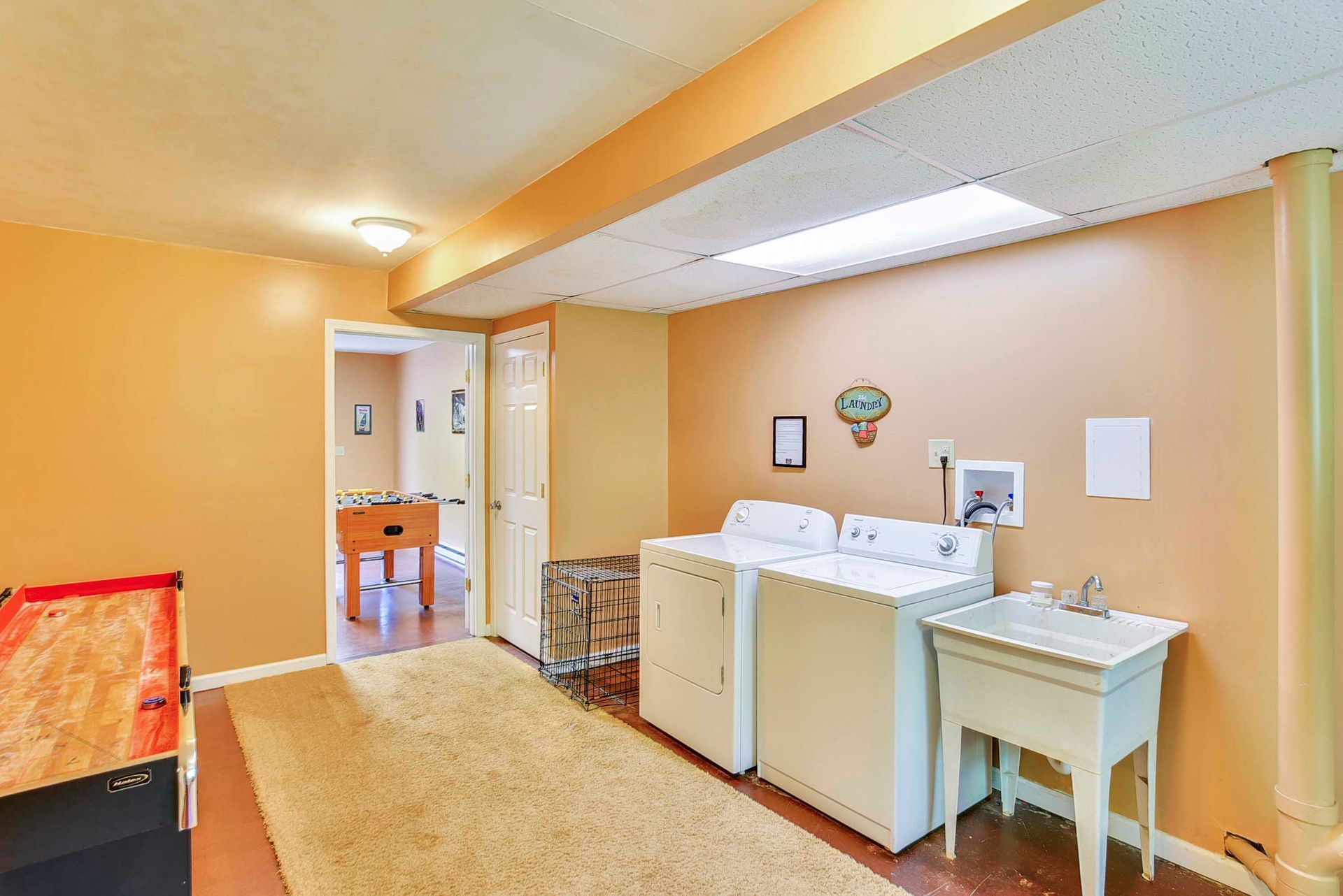 Laundry room with a washing machine, dryer, sink, and doorway to a game room.