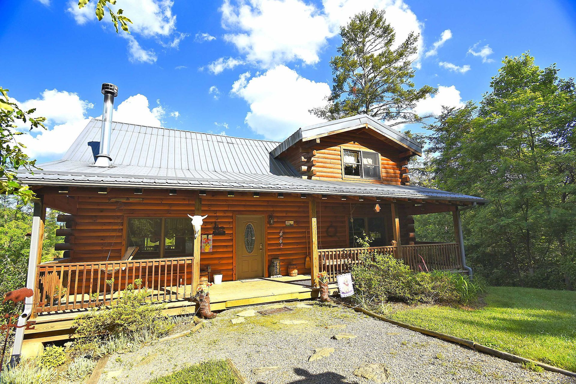 Log cabin with porch and gravel driveway under a blue sky.