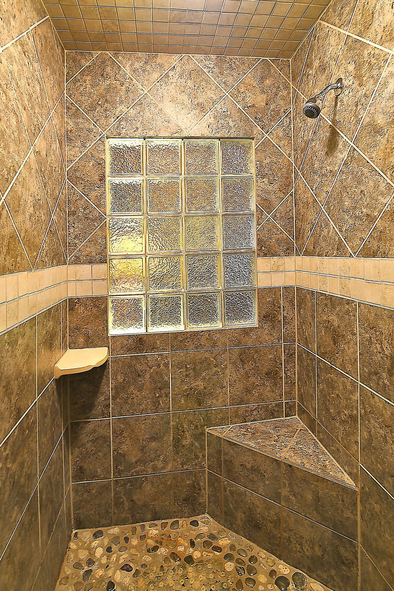Shower with stone tile walls, glass block window, built-in bench, and a showerhead.
