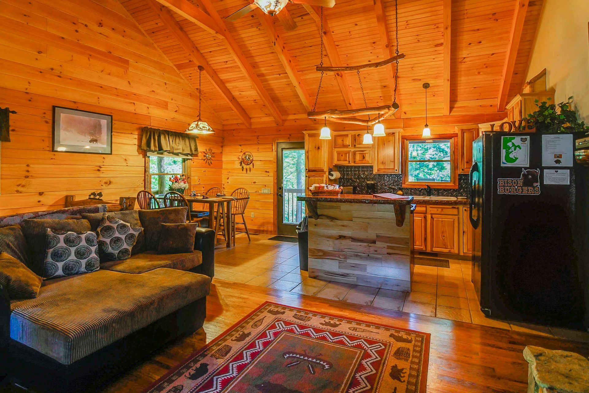 Cozy cabin interior with wooden walls, open kitchen, and living area with a brown couch and rug.