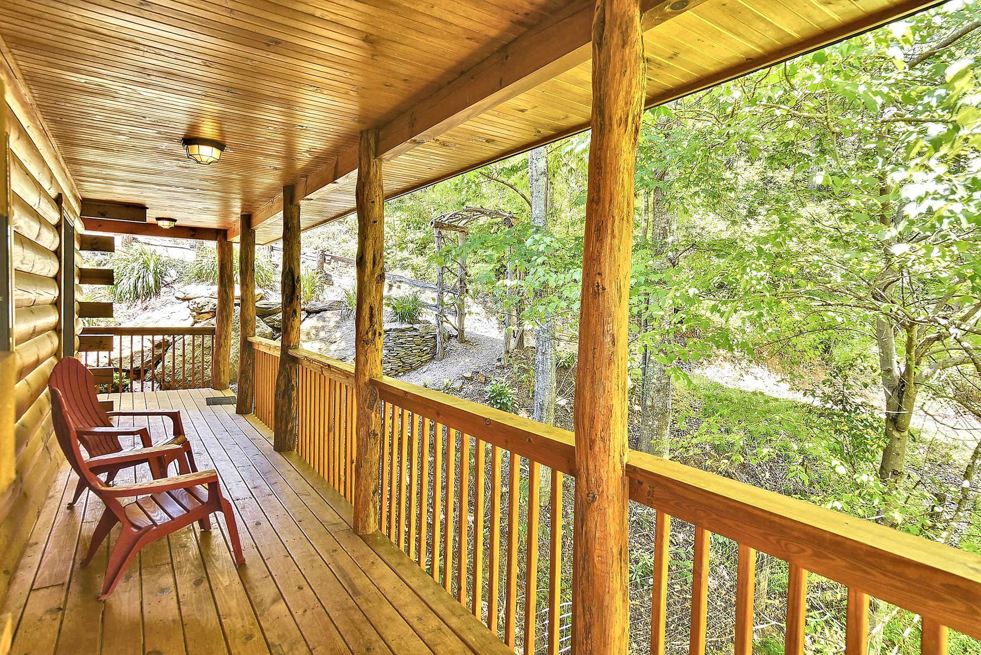 Wooden porch with two red chairs overlooking a lush green forest.