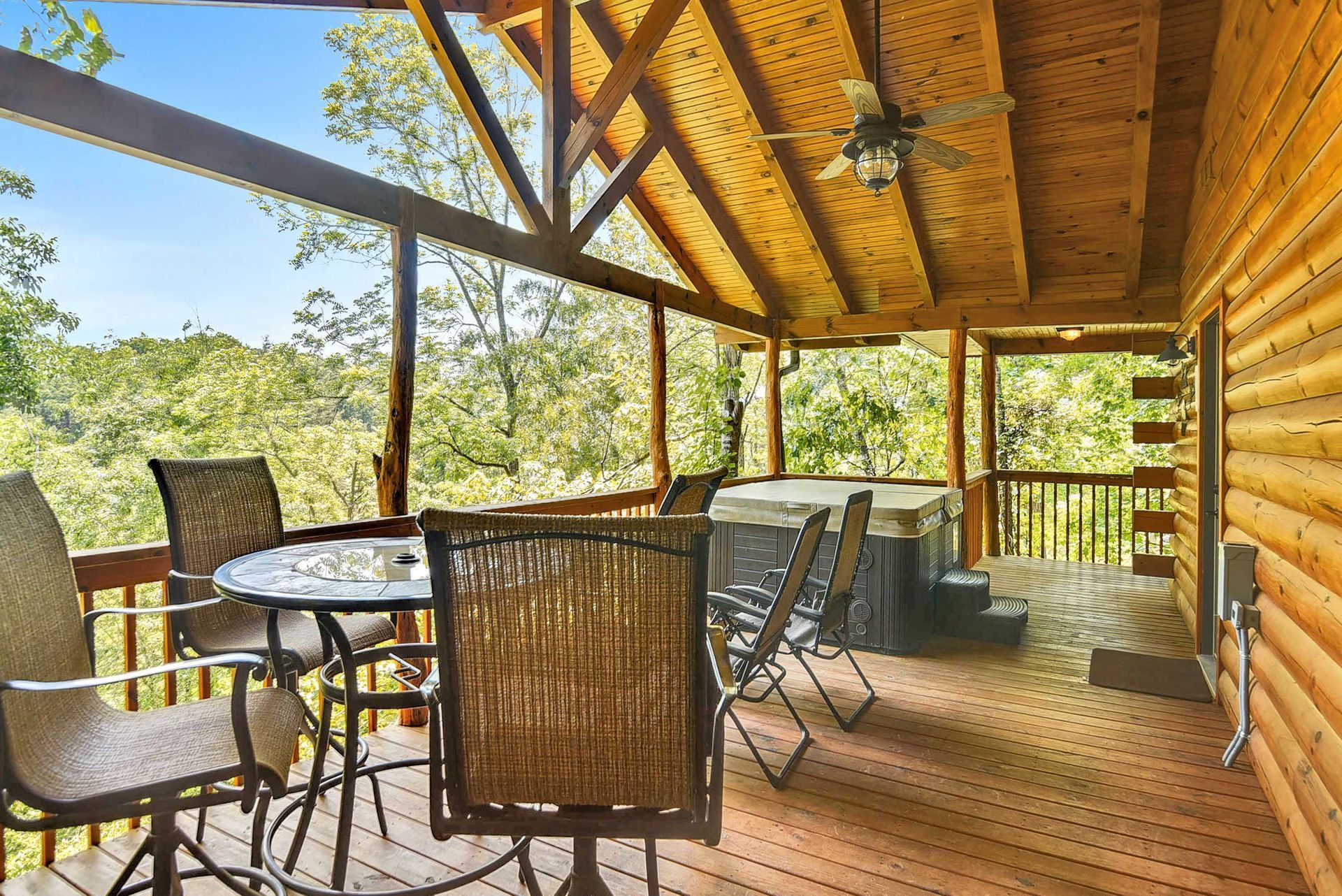 Covered wooden porch with a hot tub, table, chairs, and a view of trees.