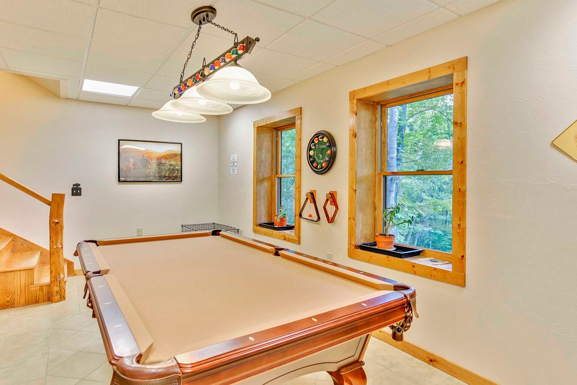 Pool table in a room with wood-framed windows, staircase, and hanging light.