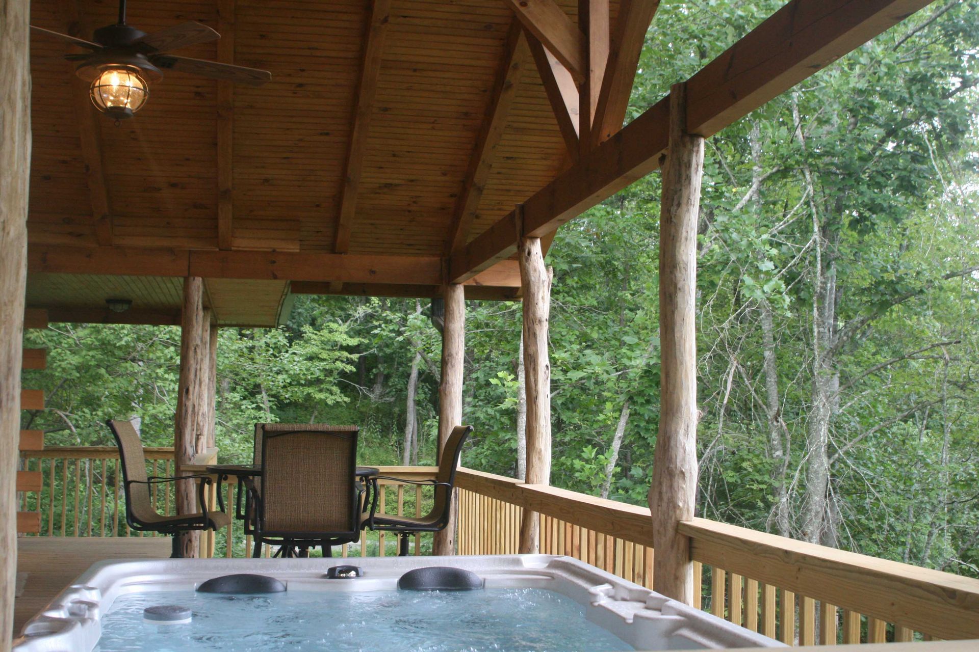 A covered porch with a hot tub, seating, and a view of trees.