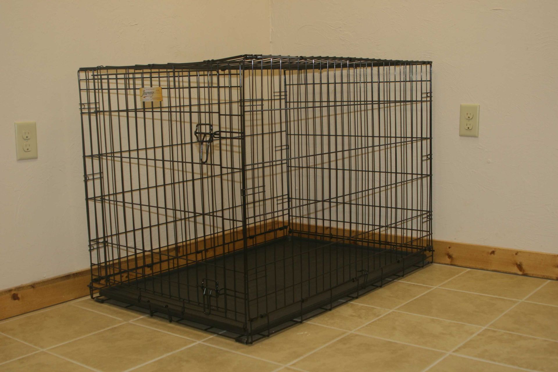 Black metal dog crate in the corner of a room with beige tile floor and white walls.