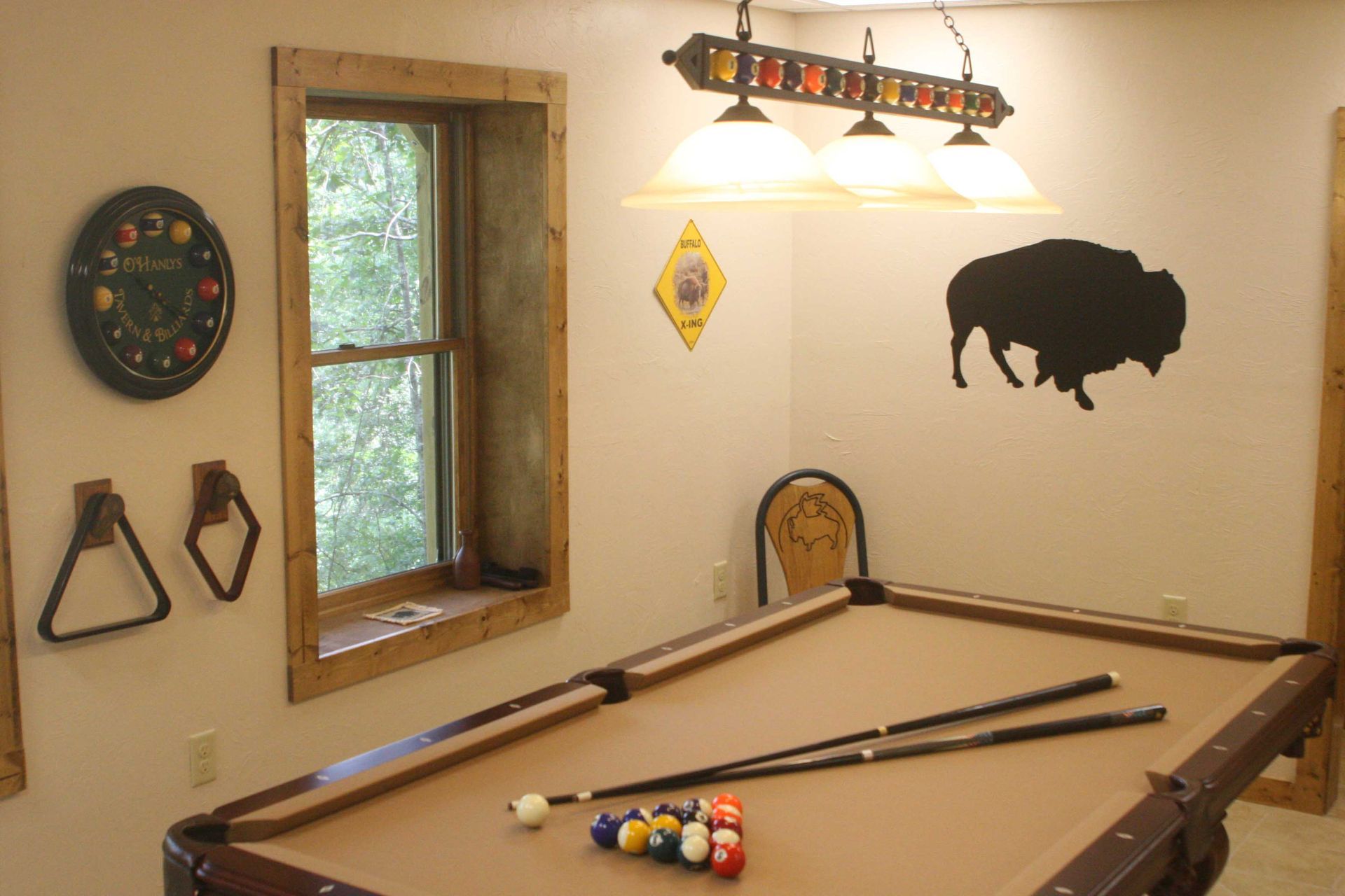 Pool table in a game room with a window, buffalo silhouette, and triangle rack.