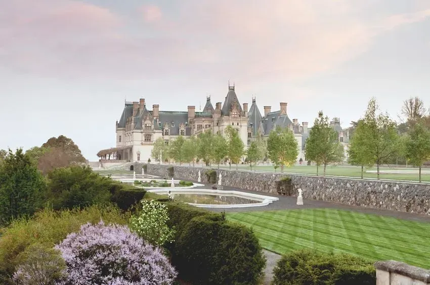 Biltmore Estate with formal gardens and a stone wall under a pastel sky.
