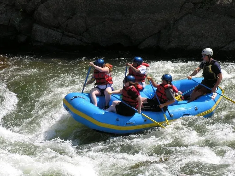 Rafting on a river with five people paddling; blue raft, rushing water, helmets.