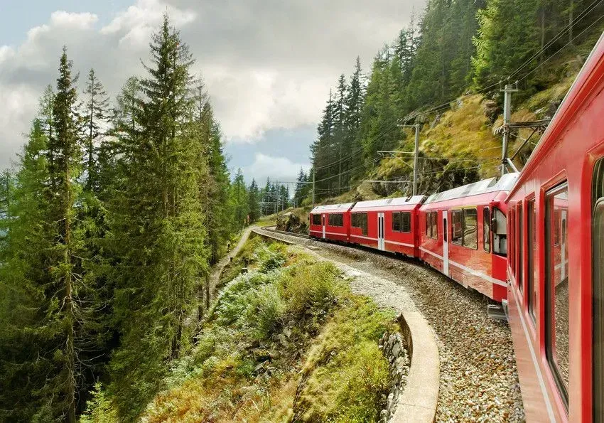 Red train winding through a lush, green mountain landscape.