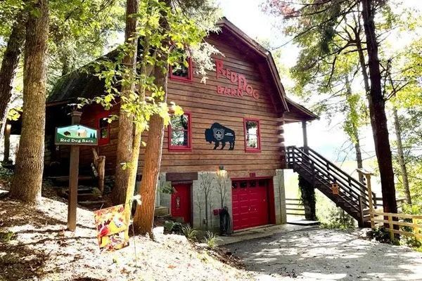 Rustic cabin with red accents and buffalo artwork, nestled in a wooded setting.