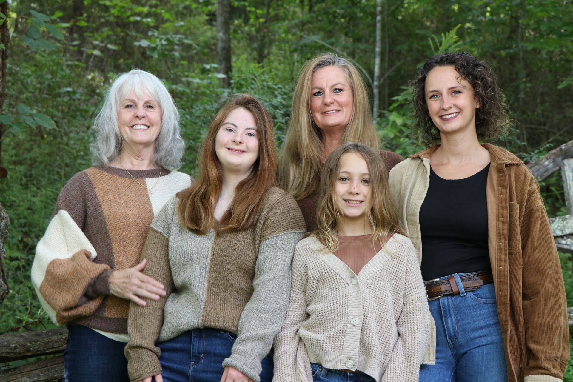 Five people stand outdoors: two older women, two younger women, and a child. All are wearing neutral-toned sweaters.