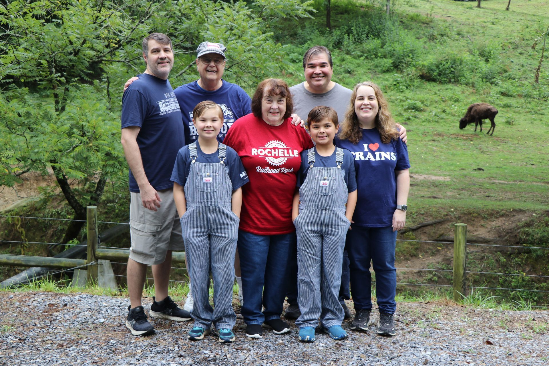Family posing outdoors; adults and children. Some wearing overalls. Mountain background.