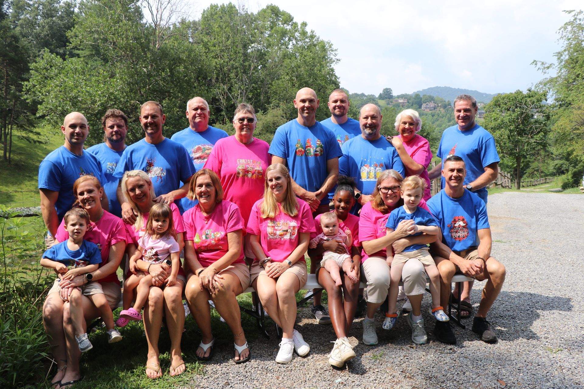 Group of people posing outdoors; some in blue shirts, some in pink, smiling.