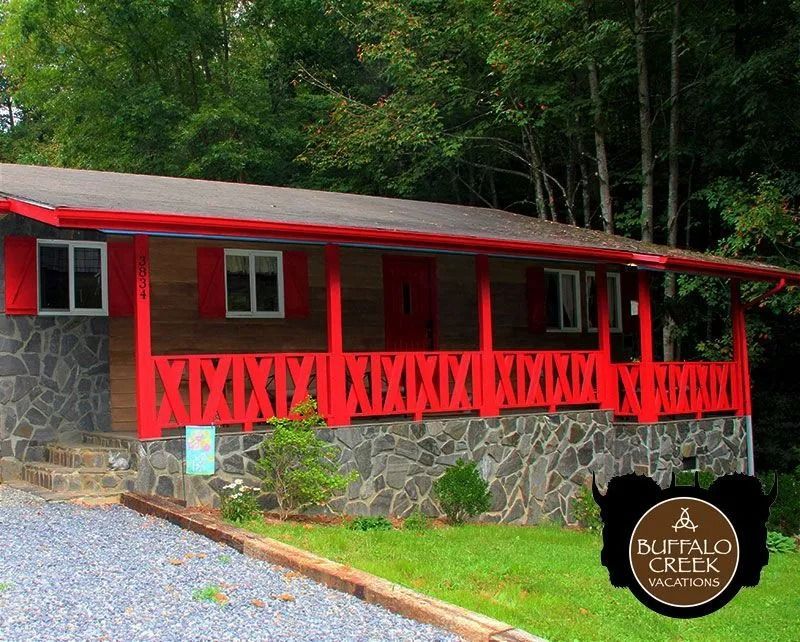 Cabin with red accents and stone foundation in a wooded setting; Buffalo Creek Vacations logo.