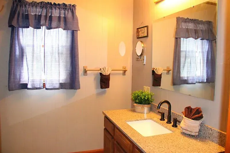 Bathroom with window, mirror, and vanity. Gray walls, blue curtains, light granite countertop, and brown towels.