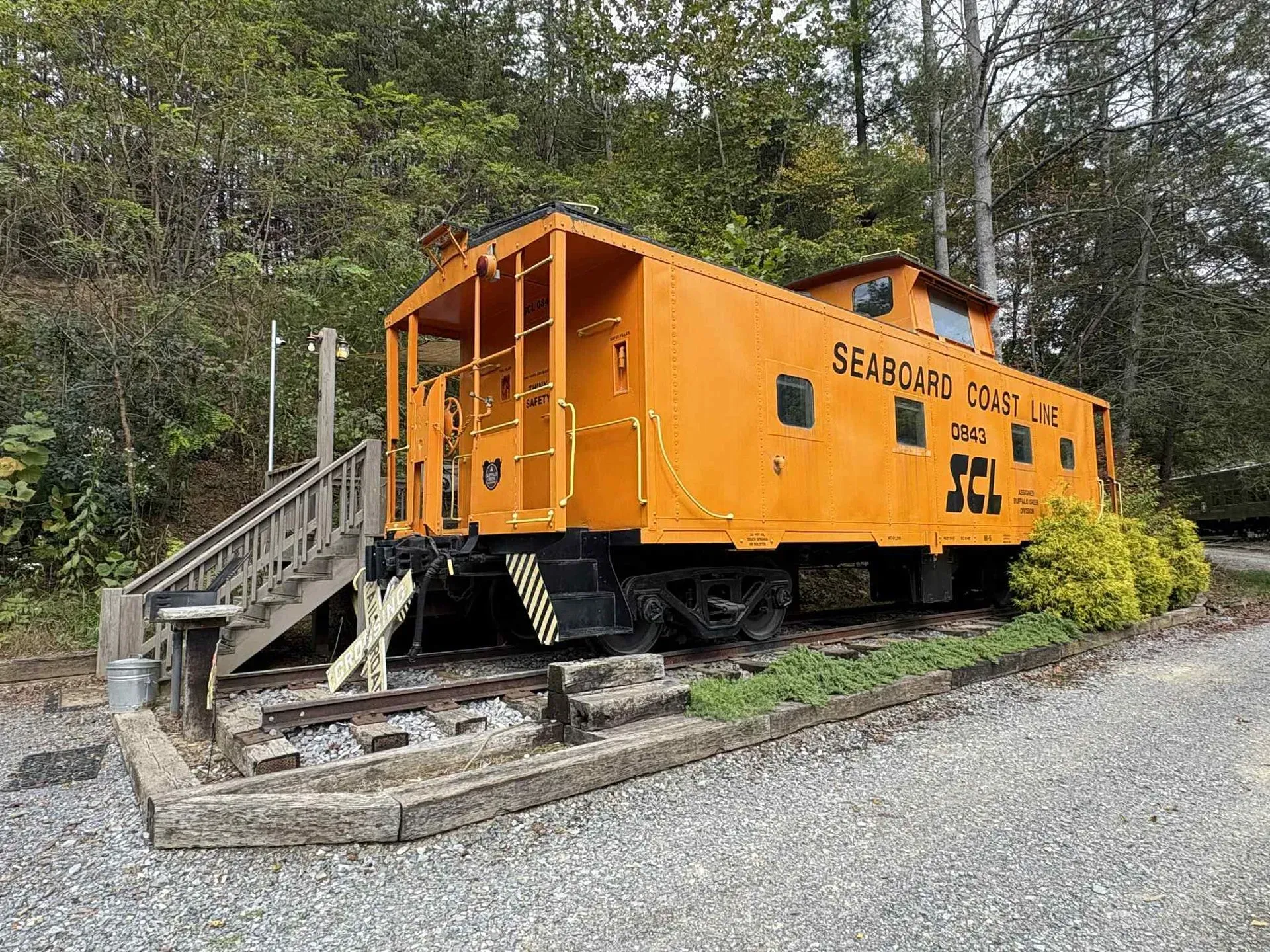 Orange train caboose on tracks, with wooden steps leading up. Located outdoors.