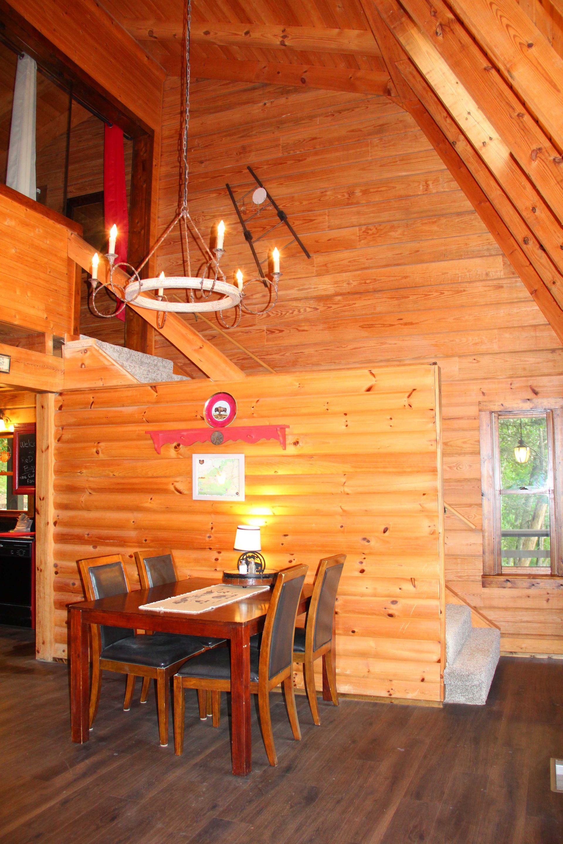 Wooden cabin dining area with table, chairs, chandelier, and window.