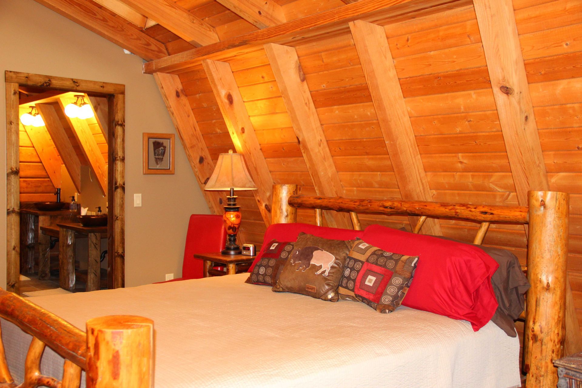 Bedroom with wooden panel walls, log bed frame, and pillows. Doorway to another room visible.