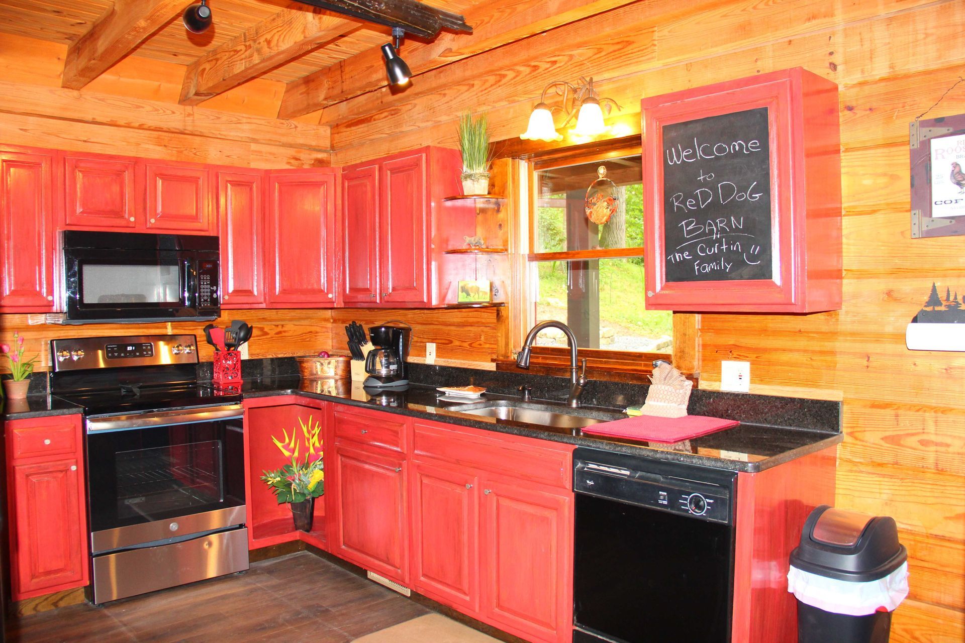 Red kitchen cabinets in a log cabin with stainless steel appliances and a blackboard.