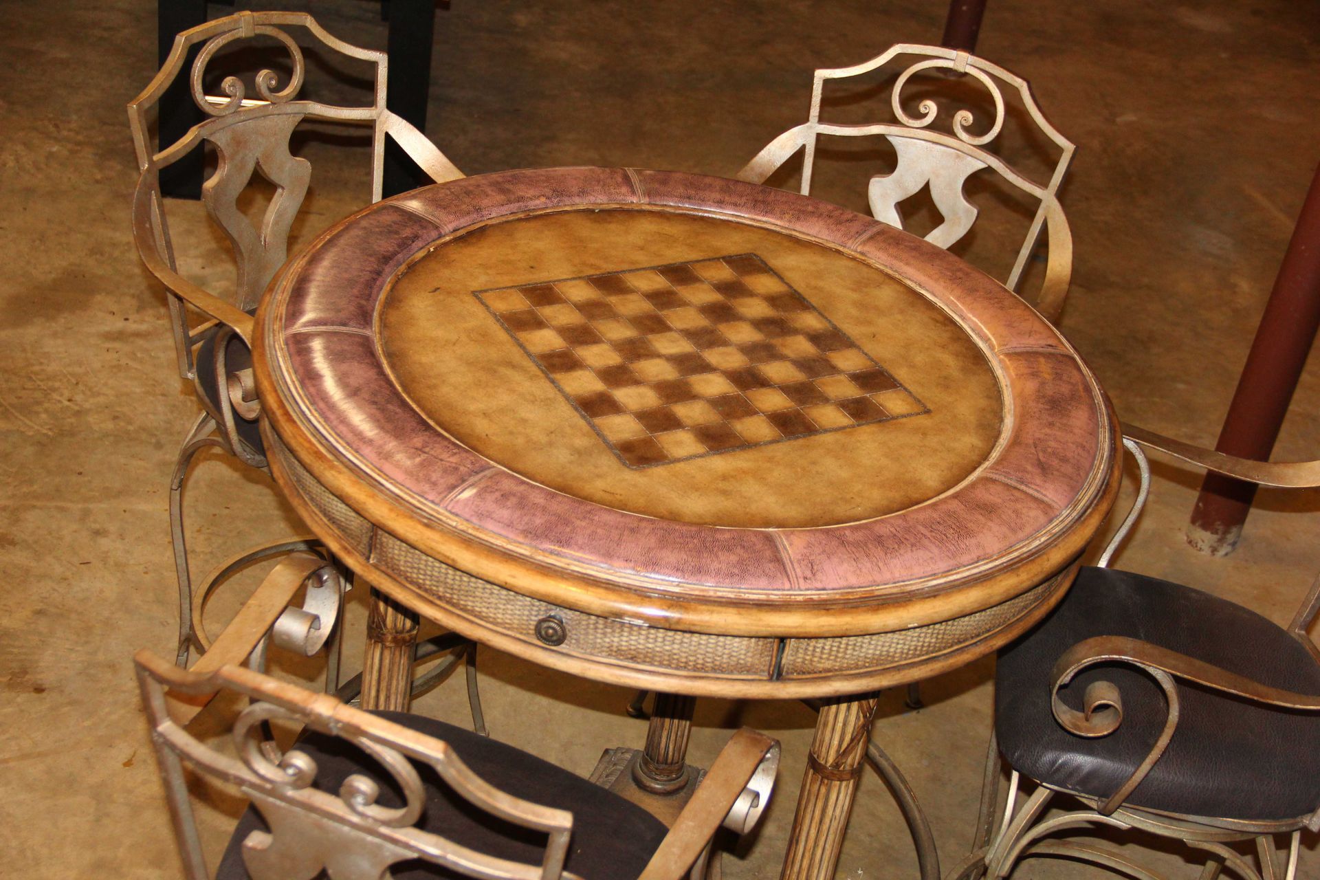 Round table with built-in chessboard, surrounded by ornate metal chairs, indoor setting.