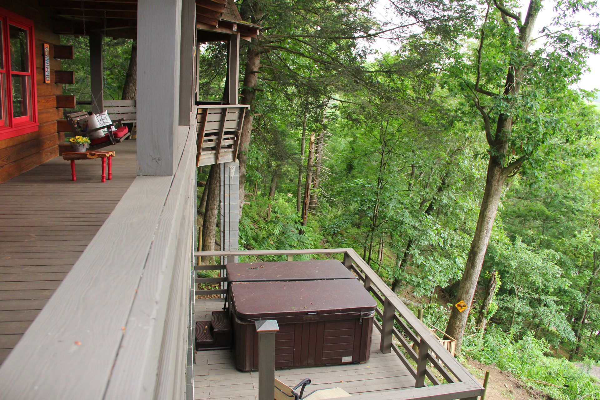 Wooden cabin with a hot tub on a balcony overlooking a lush green forest.