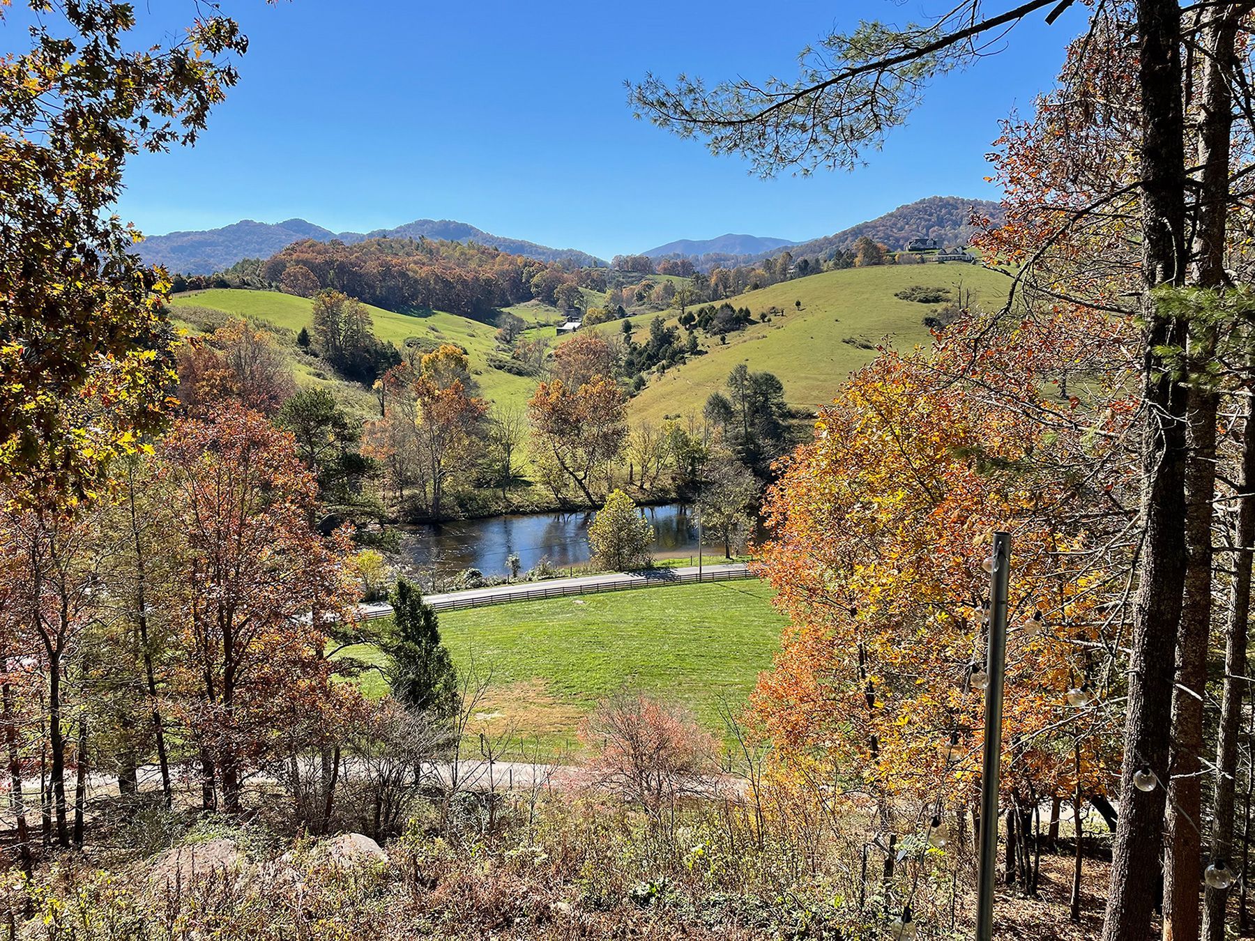 Rolling green hills with autumn trees and a pond under a blue sky.