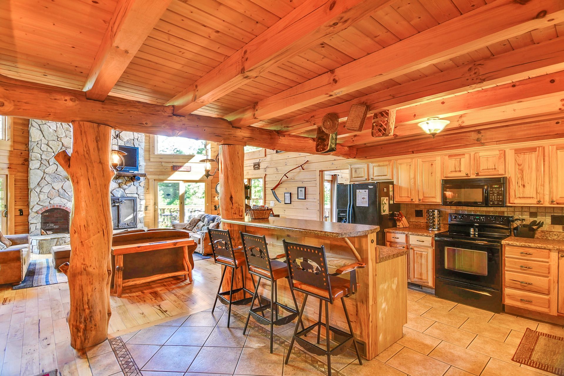Rustic kitchen with bar stools, wood beams, and a stone fireplace.