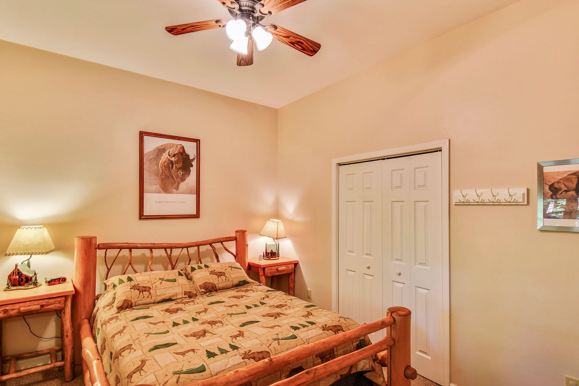 Bedroom with a wooden bed, bedside tables, and a closed closet. Beige walls and ceiling fan.