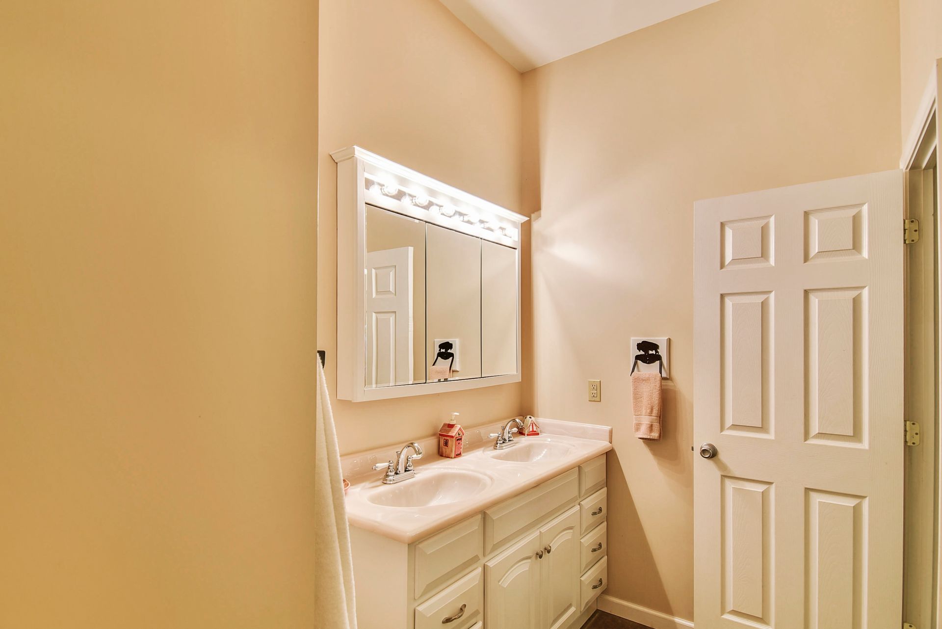 Bathroom with double vanity, mirror, and closed door, all in shades of cream and white.