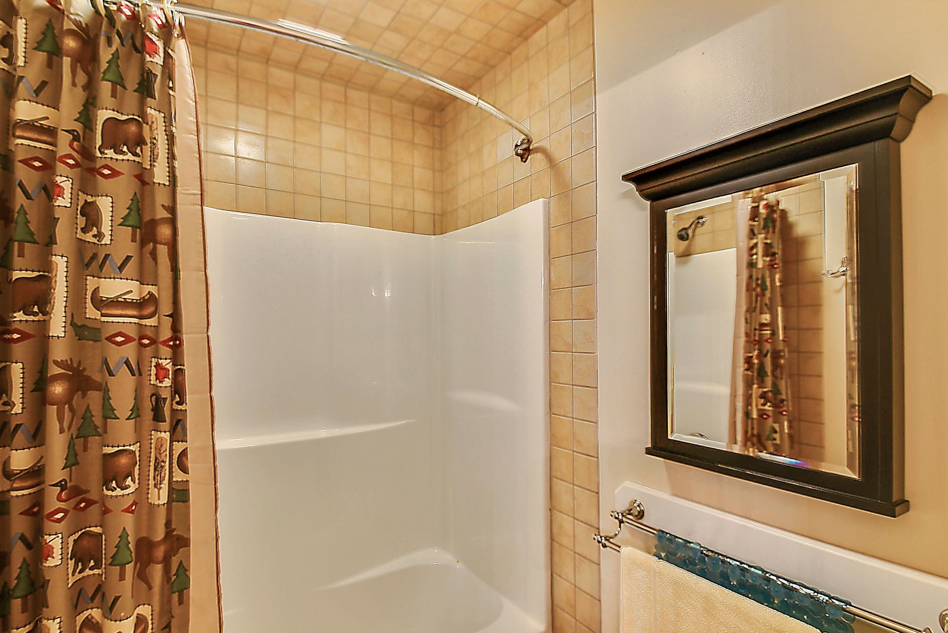 Bathroom with white shower stall, tan tile, dark framed mirror, and bear-themed shower curtain.