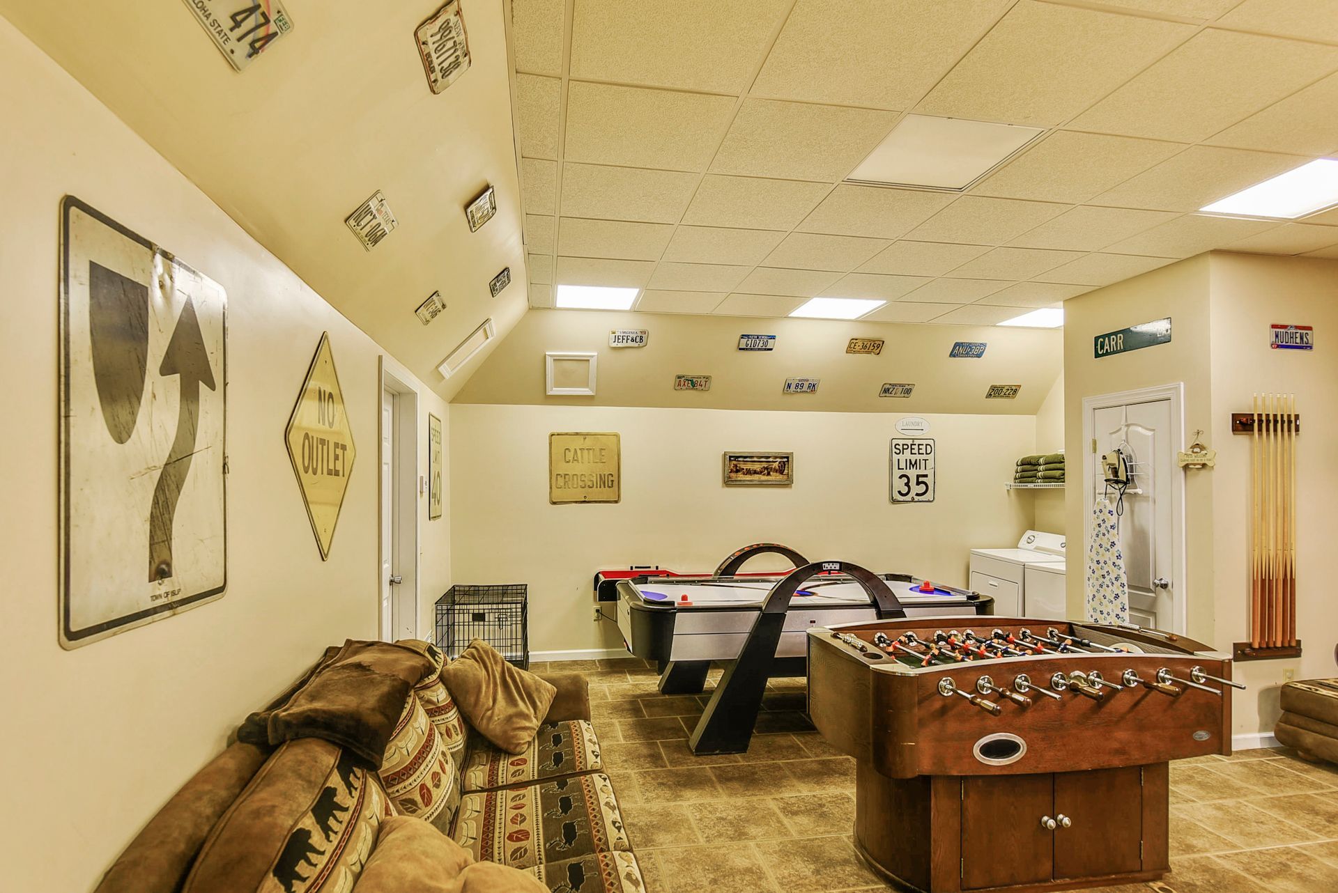 Game room with foosball and air hockey tables, sofa, signs on walls and ceiling.