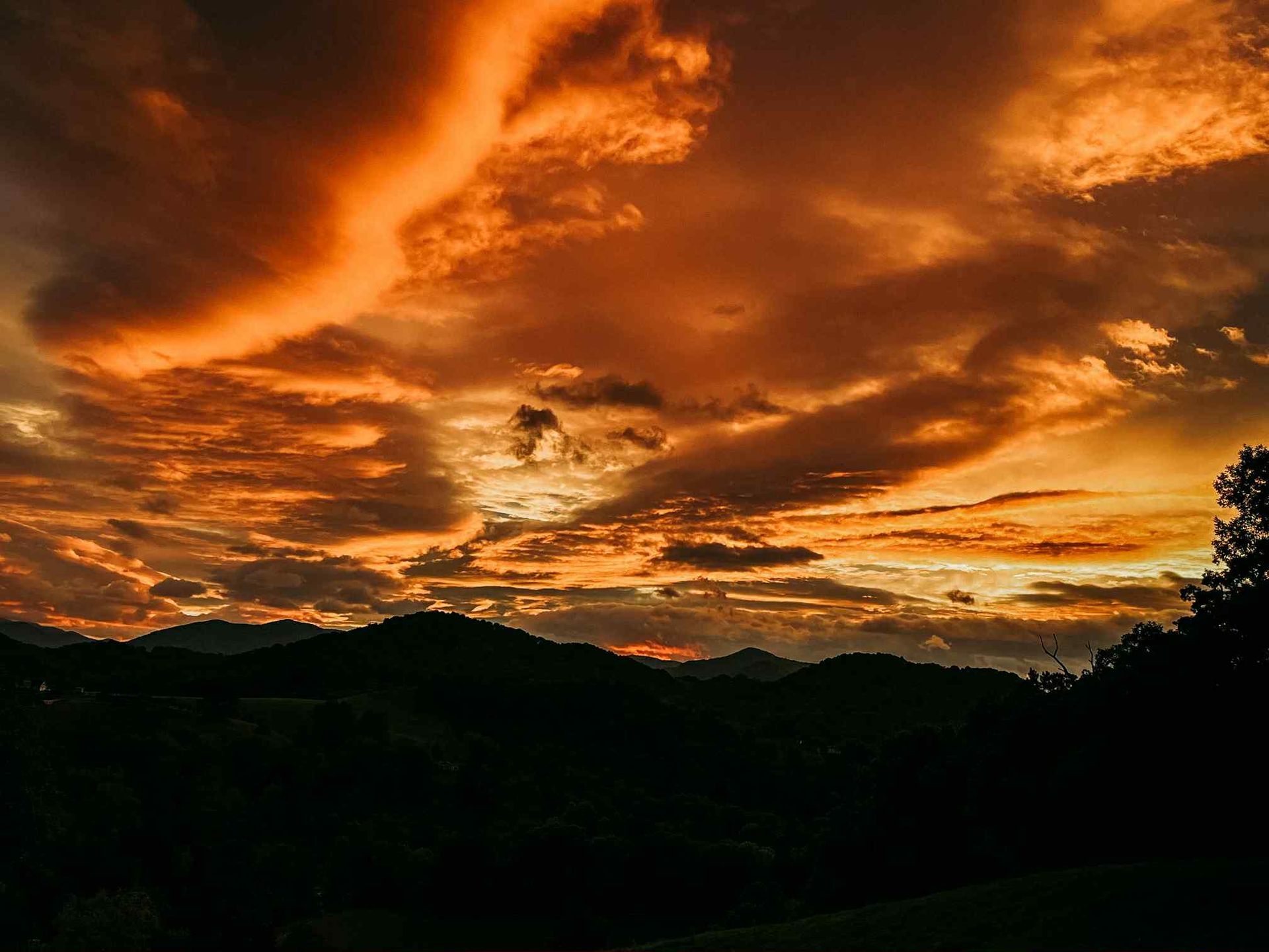 Fiery sunset over dark mountains, with vibrant orange and yellow clouds.