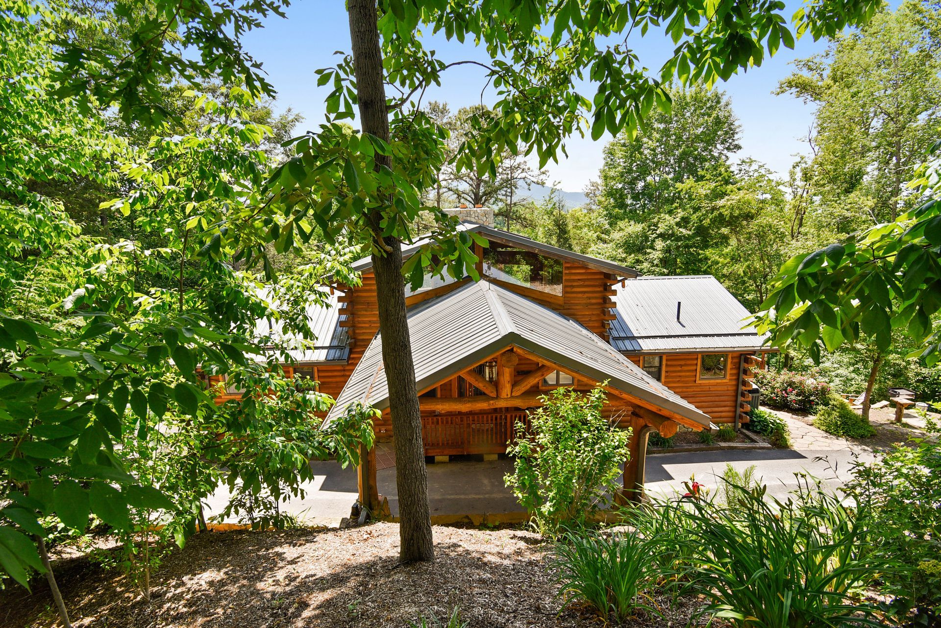 Log cabin nestled in lush greenery, featuring a covered porch with a gravel driveway.