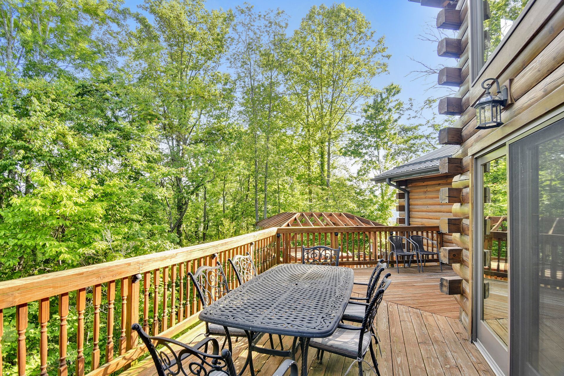 Wooden deck with patio furniture surrounded by trees and a log cabin.