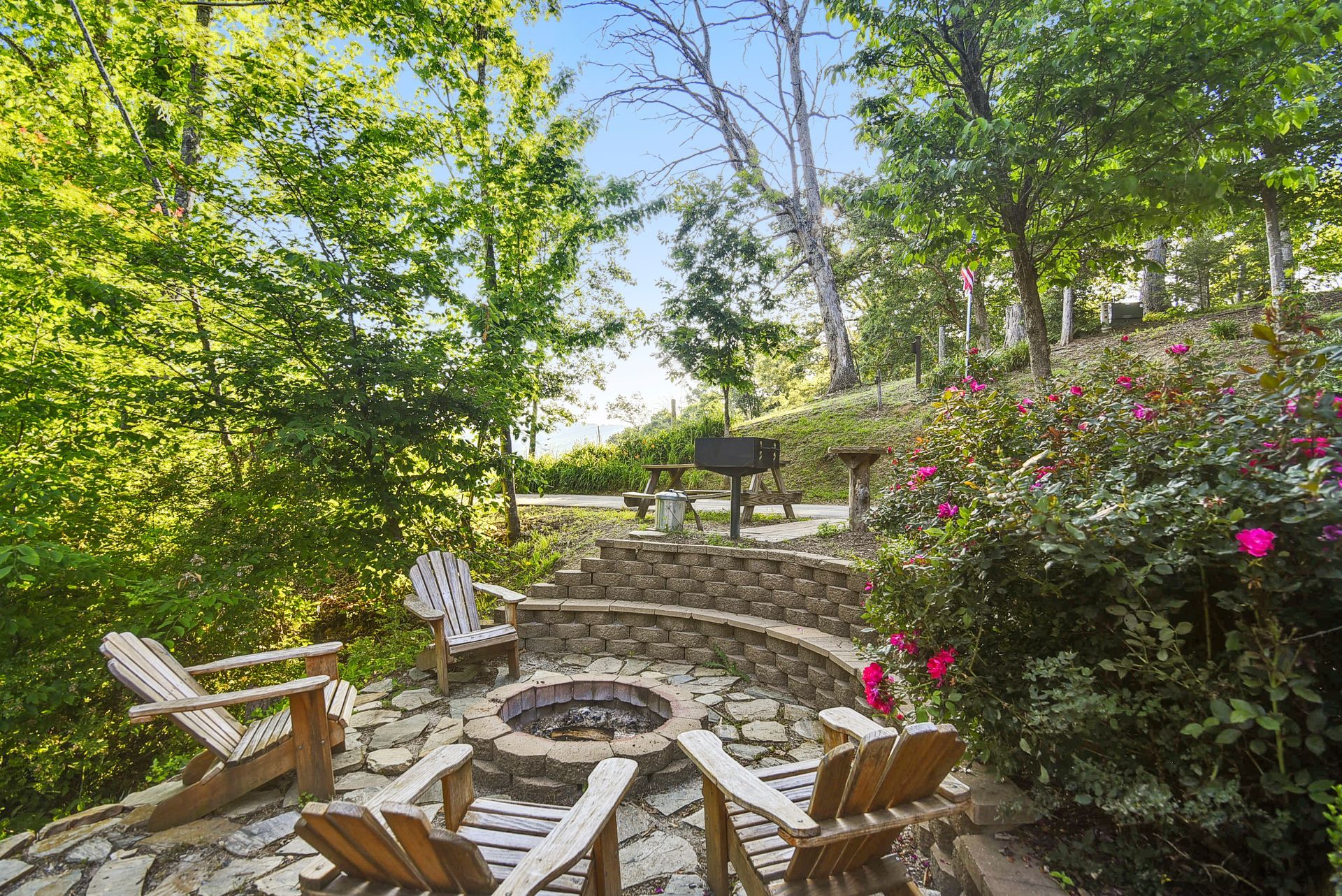 Fire pit area with wooden chairs in a lush green setting.