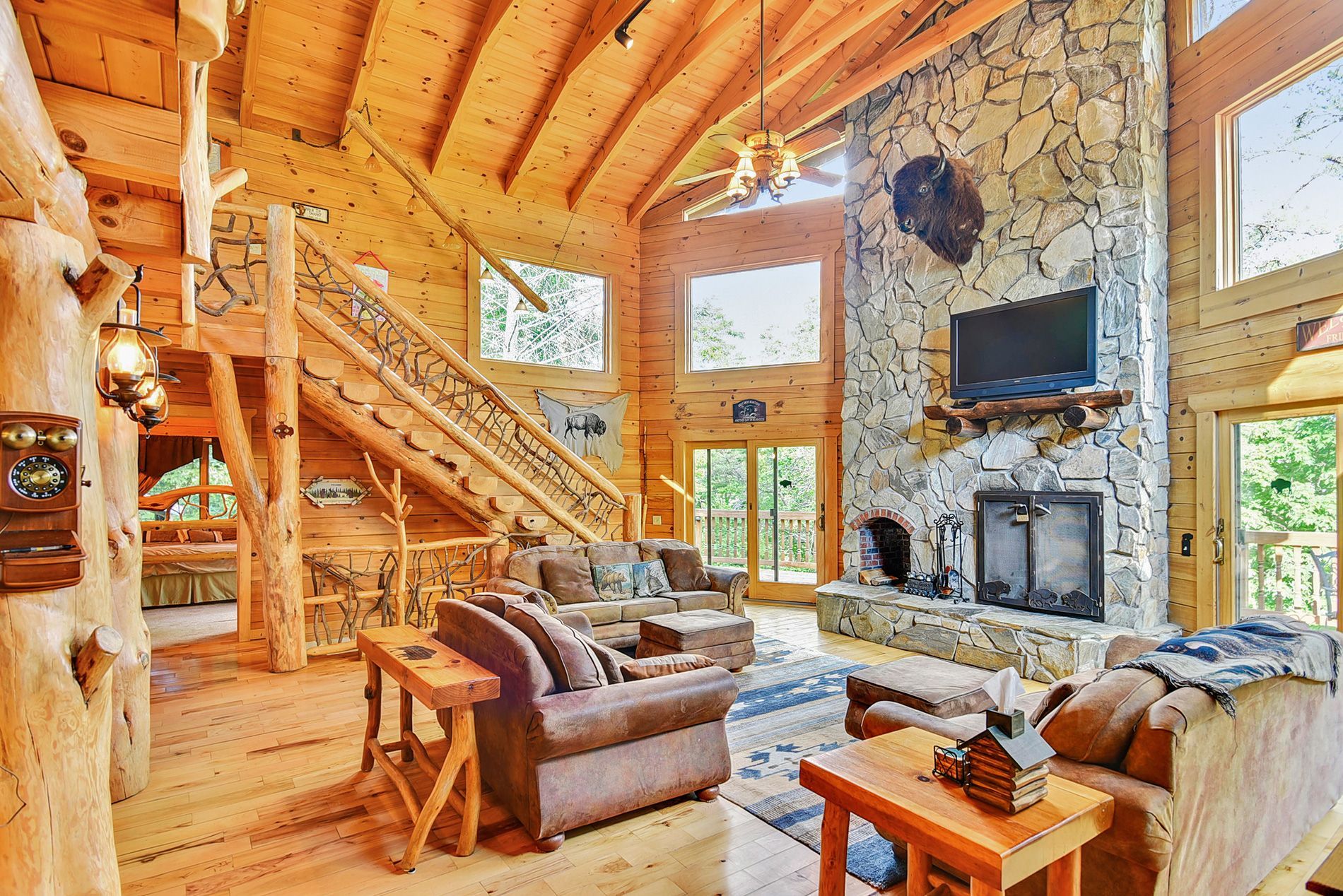 Rustic living room with stone fireplace, wooden beams, and a staircase.