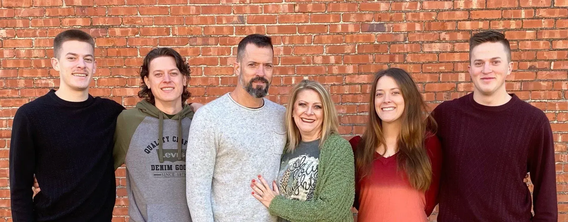 A family is posing for a picture in front of a brick wall.