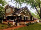 A large brown house with a porch and trees in the background