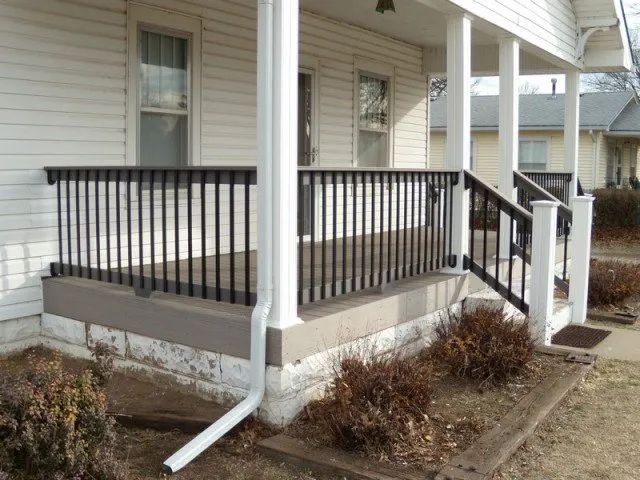 A white house with a porch with a black railing and stairs