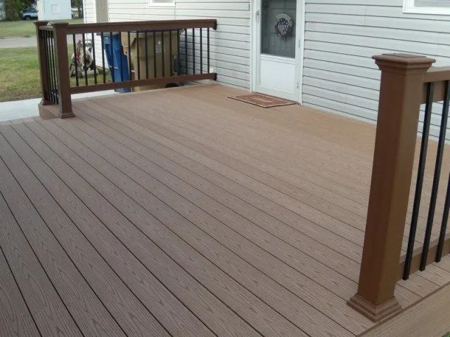 A wooden deck with a black railing is in front of a house