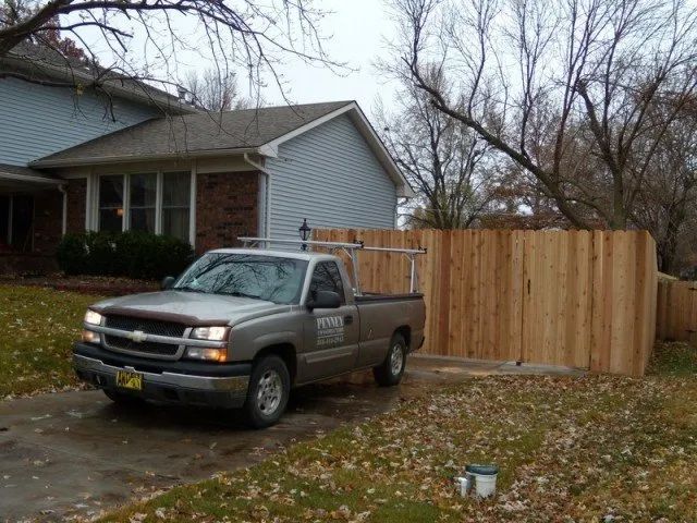 A truck is parked in front of a house with a wooden fence