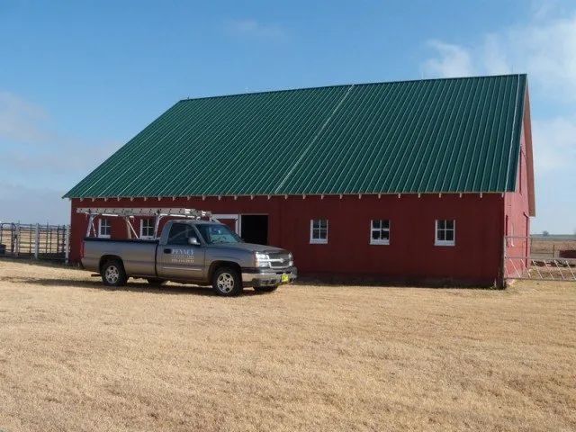 A truck is parked in front of a red barn