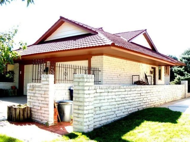 A white house with a red roof and a brick wall