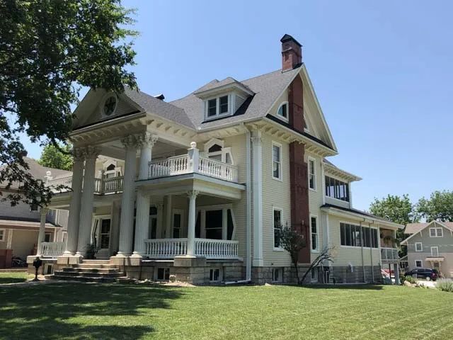 A large white house with a brick chimney sits on a lush green lawn