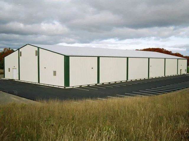 A large white building with green trim sits in the middle of a grassy field