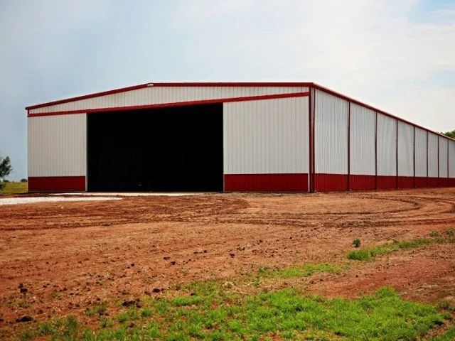 A large building with a sliding door is in the middle of a dirt field