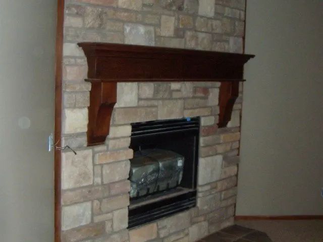 A stone fireplace with a wooden mantle in a living room