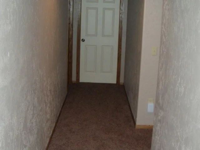 A long hallway with a white door and brown carpet