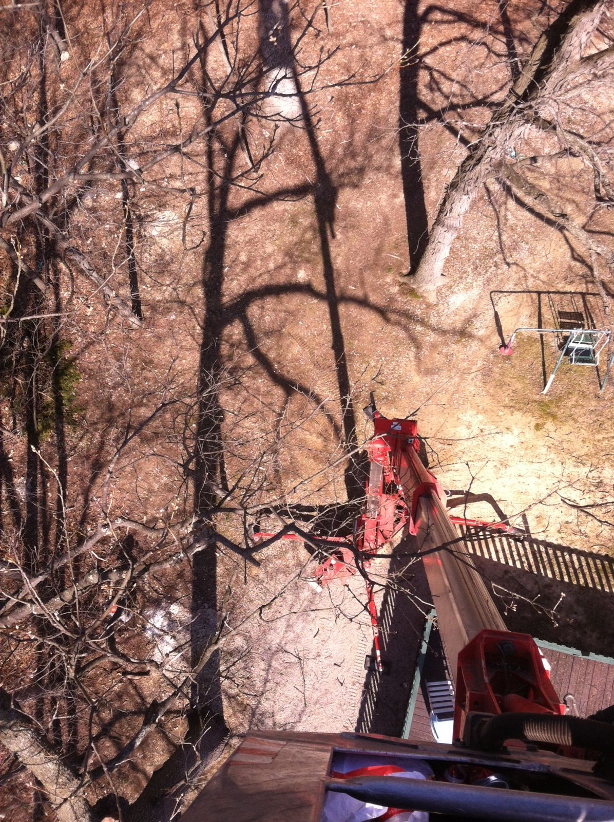 A high-angle view looking down from a rooftop at bare trees, a red climbing harness, and a swing set below.