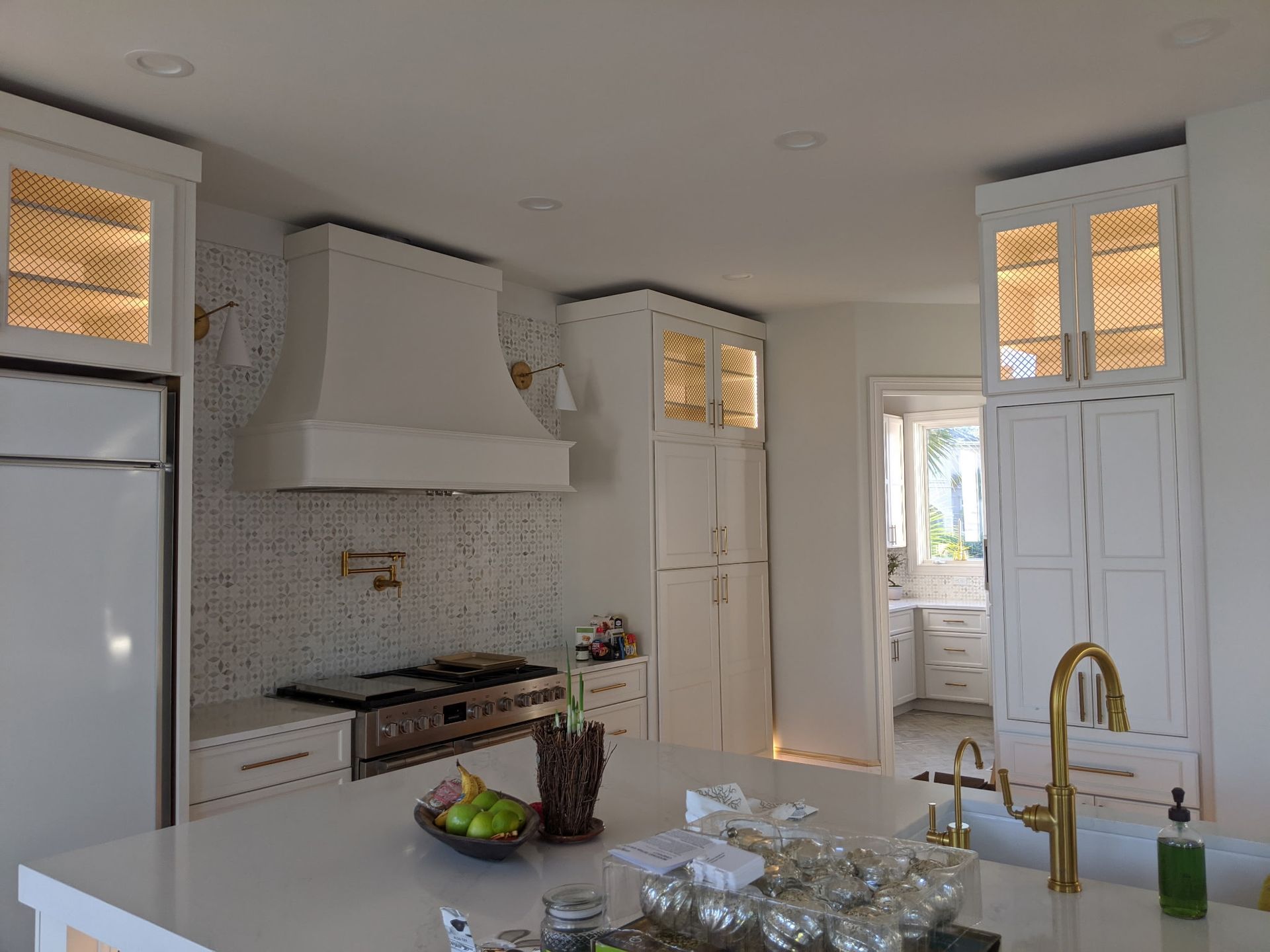 White kitchen with gold accents and a range hood over a stove.